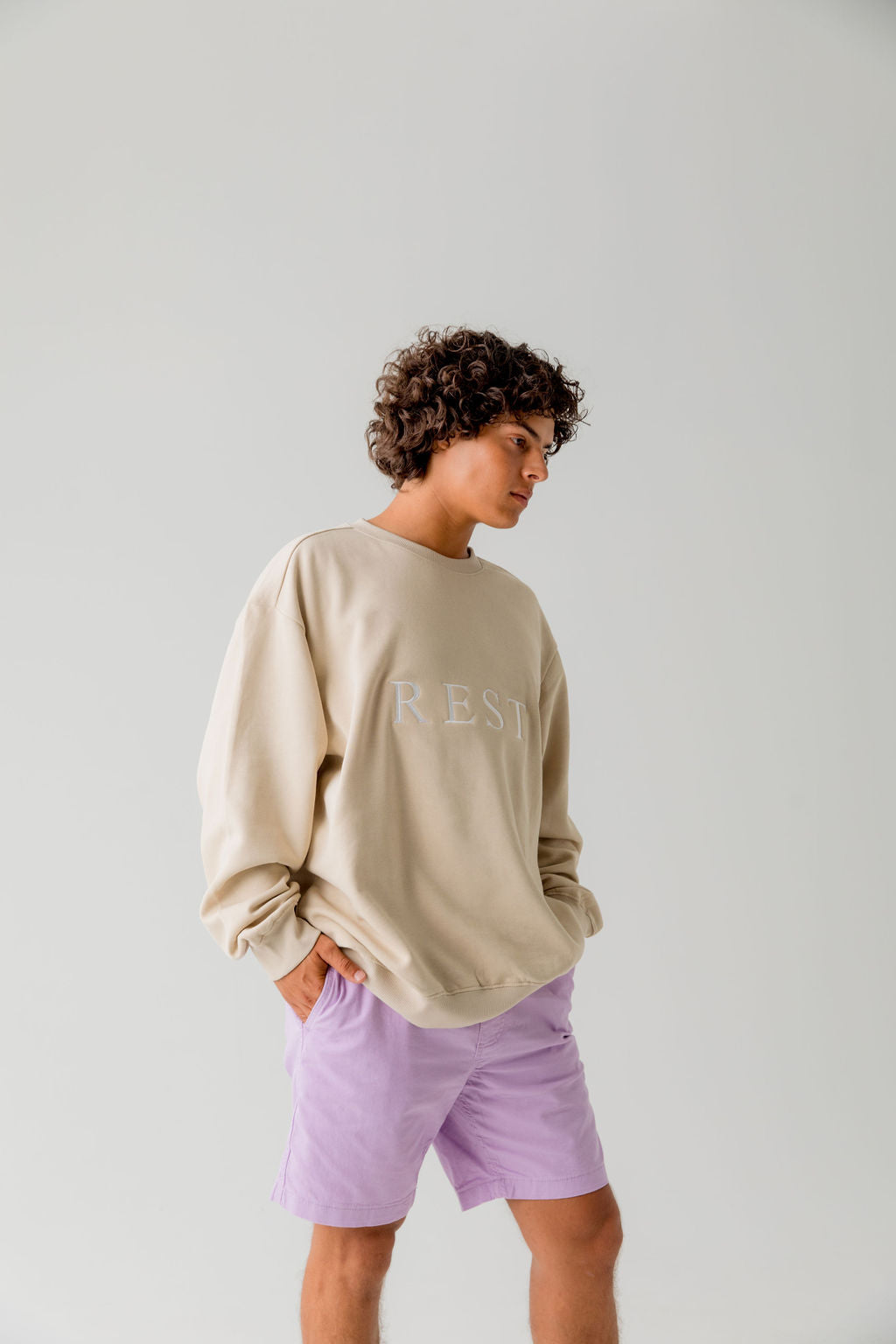 man wearing Unisex beige pullover cotton sweatshirt with " rest" embroidered in white