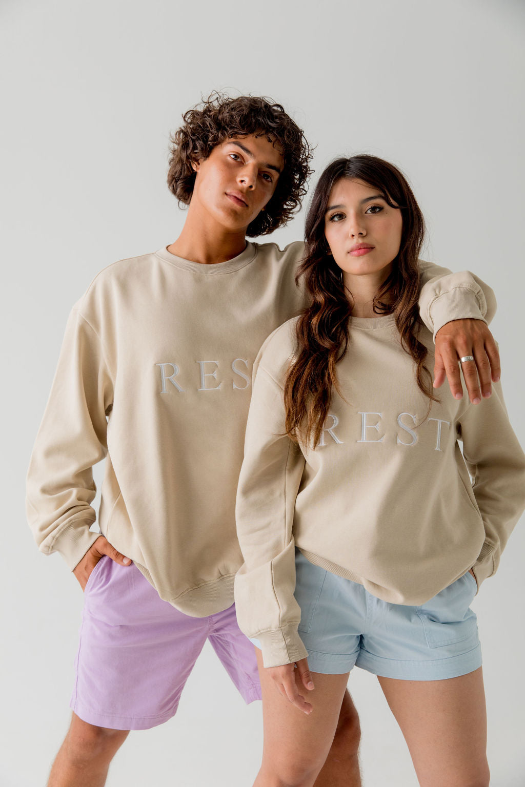 man and woman wearing Unisex beige pullover cotton sweatshirt with " rest" embroidered in white